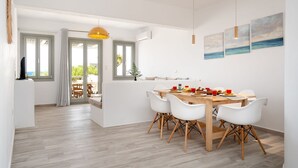 Een moderne eetruimte met een houten tafel, witte stoelen, een gele hanglamp en uitzicht op het buitenleven door grote ramen.