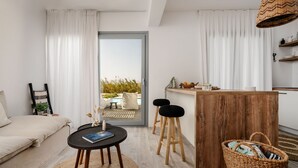 Un espacio habitable moderno con un sofá, una pequeña mesa redonda y una cocina con taburetes y una encimera de madera.