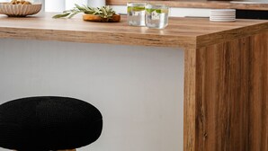 Una cocina con encimera de madera, un taburete negro, un microondas, un hervidor y una lámpara colgante.