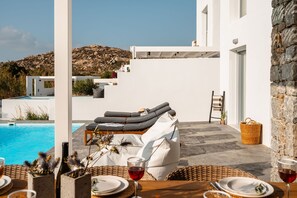 A poolside area with a lounge chair, dining table, and a view of a mountainous landscape. - Maison Solea Plaka With 3 Bedrooms and 3 Bathrooms (Naxos)
