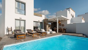 Un área de piscina moderna con sillones reclinables y una pared de piedra.