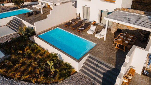 Una villa moderna con piscina, mobiliario exterior y un muro de piedra.