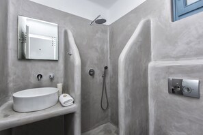 Une salle de bain moderne avec un grand lavabo ovale, un miroir, une douche équipée d’un pommeau de douche à main et un panneau de commande fixé au mur.