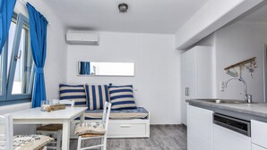 Une cuisine compacte dotée d’un lave-vaisselle intégré, d’une table à manger avec des chaises et d’un petit coin salon avec un canapé et des coussins.