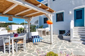 Un bâtiment blanc avec une porte bleue, un sol en pierre et des sièges à l’extérieur.