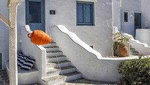 Un bâtiment blanc avec des portes et des fenêtres bleues, un escalier en pierre et un pot orange suspendu.