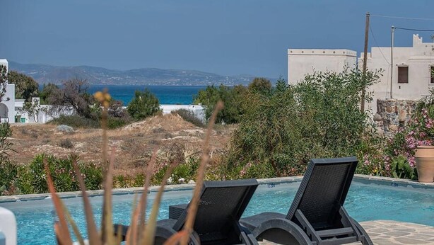 A poolside area with two lounge chairs, a view of the sea, and a building in the background. - 293102 - Casa Magnifica (Naxos)