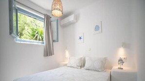 A bedroom with a bed, a window with curtains, a wall-mounted air conditioner, and a bedside table with a lamp. - 293102 - Casa Magnifica (Naxos)