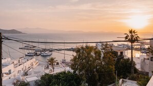 A marina with boats docked, surrounded by buildings and palm trees, with a sunset in the background. - Kastro Suite in Naxos-chora (Naxos)
