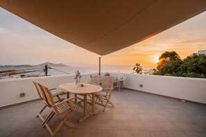 A wooden table and chairs on a terrace with a view of the sea and mountains during sunset. - Kastro Suite in Naxos-chora (Naxos)