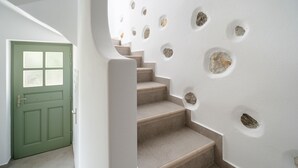 A staircase with beige steps leading to a landing, surrounded by a white wall with circular stone insets. - Kastro Suite in Naxos-chora (Naxos)