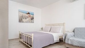 A bedroom with a bed, a couch, and a painting of a beach scene. - Kastro Suite in Naxos-chora (Naxos)
