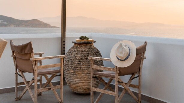 A balcony with two wooden chairs, a large vase, and a hat. - Kastro Suite in Naxos-chora (Naxos)