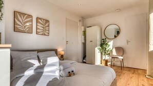 A neatly made bed with white linens, a bedside table with a lamp, and a mirror on the wall.
