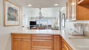 A kitchen with wooden cabinets, a large island, a coffee maker, and a view of the city. - Beach House 101D - Gulf Front Resort! (Miramar Beach)