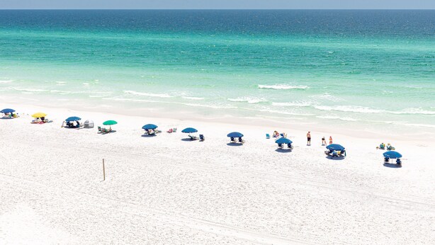 A beach with white sand and clear turquoise water. There are several umbrellas and people relaxing on the beach. - Beach House 101D - Gulf Front Resort! (Miramar Beach)