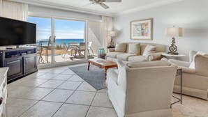 A spacious living room with a large flat-screen TV, a sofa, a coffee table, and a dining area with chairs. - Beach House 101D - Gulf Front Resort! (Miramar Beach)