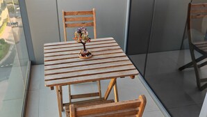 A small balcony with a wooden table and chairs, a small decorative plant, and a view of the cityscape. - Chic 1-bedroom apartment in enchanting Dubai with WiFi, fitness room (Dubai)