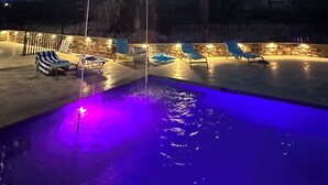 Ett poolområde som är vackert även på kvällen, med solstolar och en fontän, omgivet av stenmurar och med ett bergigt landskap i bakgrunden.