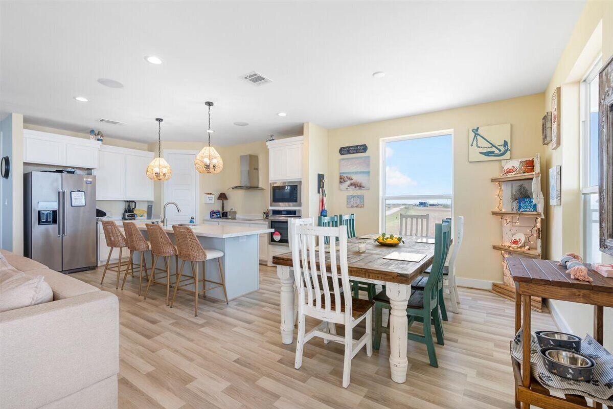 Une cuisine moderne avec des meubles blancs, un îlot central et un coin repas doté de chaises en bois.
