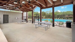 An outdoor covered patio area with picnic tables and a view of a swimming pool. - Fully-equipped home for the family (Boerne)