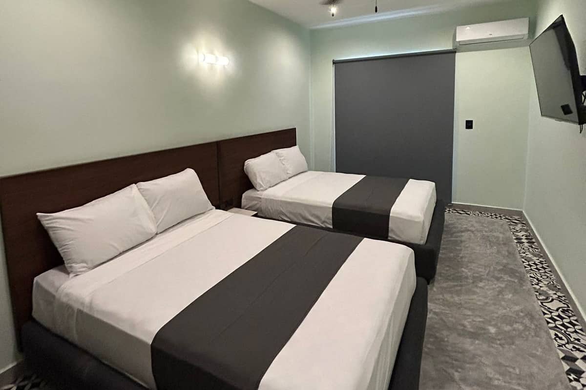 A hotel room with two beds, a ceiling fan, a TV mounted on the wall, and an air conditioning unit.