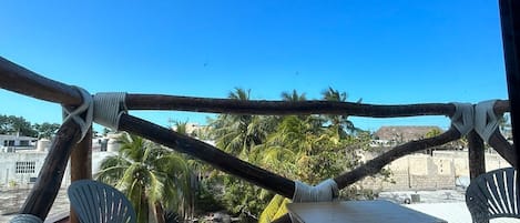 A balcony with a view of palm trees and buildings, featuring a table and chairs.