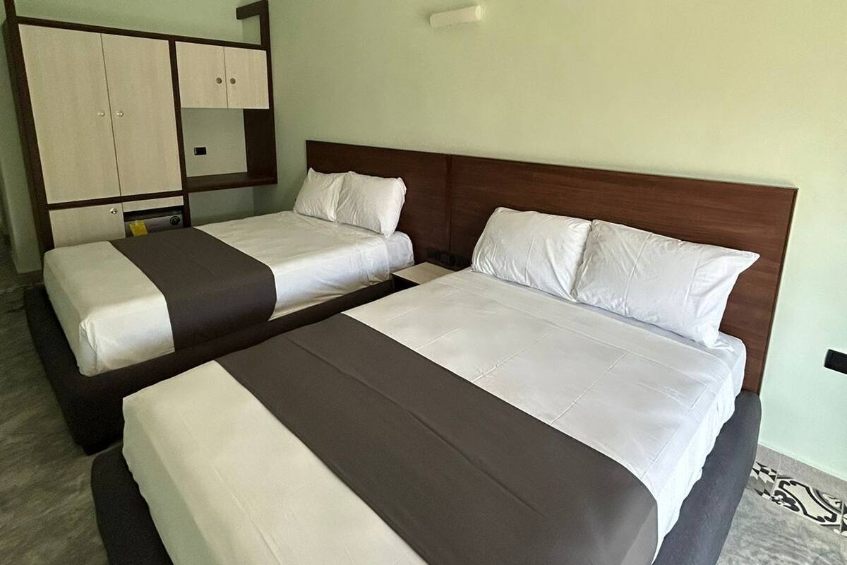 A hotel room with two beds, a ceiling fan, a wardrobe, and a light switch on the wall.