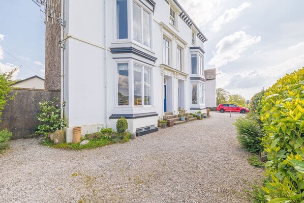 A two-story house with a gravel driveway and a red car parked in the background. - Location, views, parking (Bowness-on-Windermere)