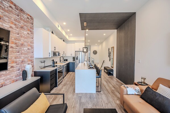 A modern kitchen with white cabinets, a central island, and a dining area with a sofa and table.
