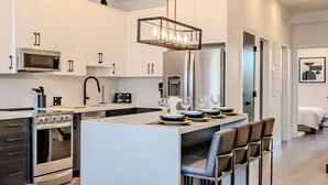 Eine moderne Küche mit weißen Schränken, Edelstahlgeräten und einer zentralen Kochinsel mit Barhocker.