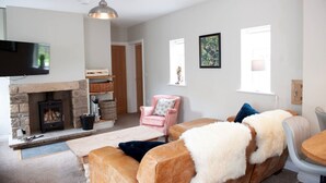 A cozy living room with a stone fireplace, a pink armchair, and a sofa with a fluffy throw. - Relaxing rural retreat (Sedbergh)