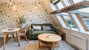 A cozy room with a green sofa, a round wooden table, and a white chair. There are two hanging light bulbs and a potted plant. - Ambleside View Ambleside, perfect for a romantic break surrounded by breath taking scenery (Ambleside)