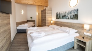 Une chambre d’hôtel avec un plafond en bois, deux lits avec du linge de lit blanc, un tableau représentant une forêt et une table de chevet avec une lampe.