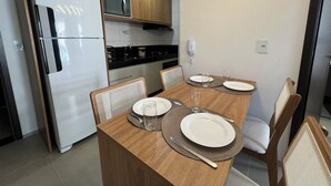 A modern kitchen with a dining table set for four, equipped with a refrigerator, microwave, and stove. - Edificio Promenade II Apt 508  (Maceió)