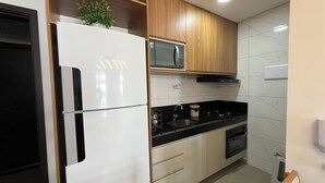 A modern kitchen with a white refrigerator, a microwave, wooden cabinets, and a black countertop. - Edificio Promenade II Apt 508  (Maceió)