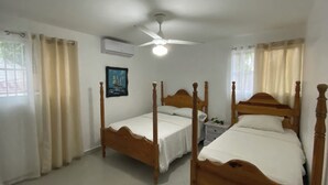A bedroom with two wooden beds, a ceiling fan, and a window with curtains. - Oceanview 5 BR w private pool, rooftop terrace & full staff 4 min from the beach (Cofresi)