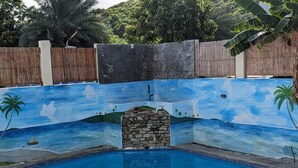 A swimming pool with a mural of a beach scene, stone steps, and white outdoor furniture. - Oceanview 5 BR w private pool, rooftop terrace & full staff 4 min from the beach (Cofresi)