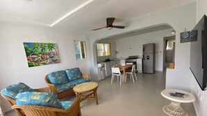 A spacious living area with a sofa, chairs, and a small table. A kitchen with a refrigerator and stove is visible in the background. - Oceanview 5 BR w private pool, rooftop terrace & full staff 4 min from the beach (Cofresi)