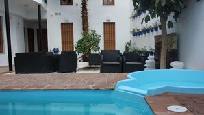 A swimming pool with a tiled deck, surrounded by outdoor furniture and potted plants. - casapatiolaspalmeras (Córdoba)
