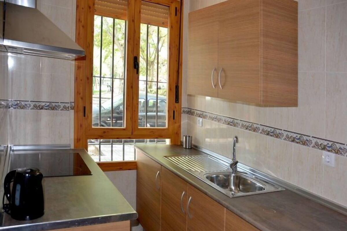 A kitchen with wooden cabinets, a stainless steel sink, and a window with blinds.