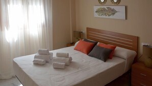 A neatly made bed with rolled towels, a wooden headboard, and a wall-mounted artwork. - casapatiolaspalmeras (Córdoba)