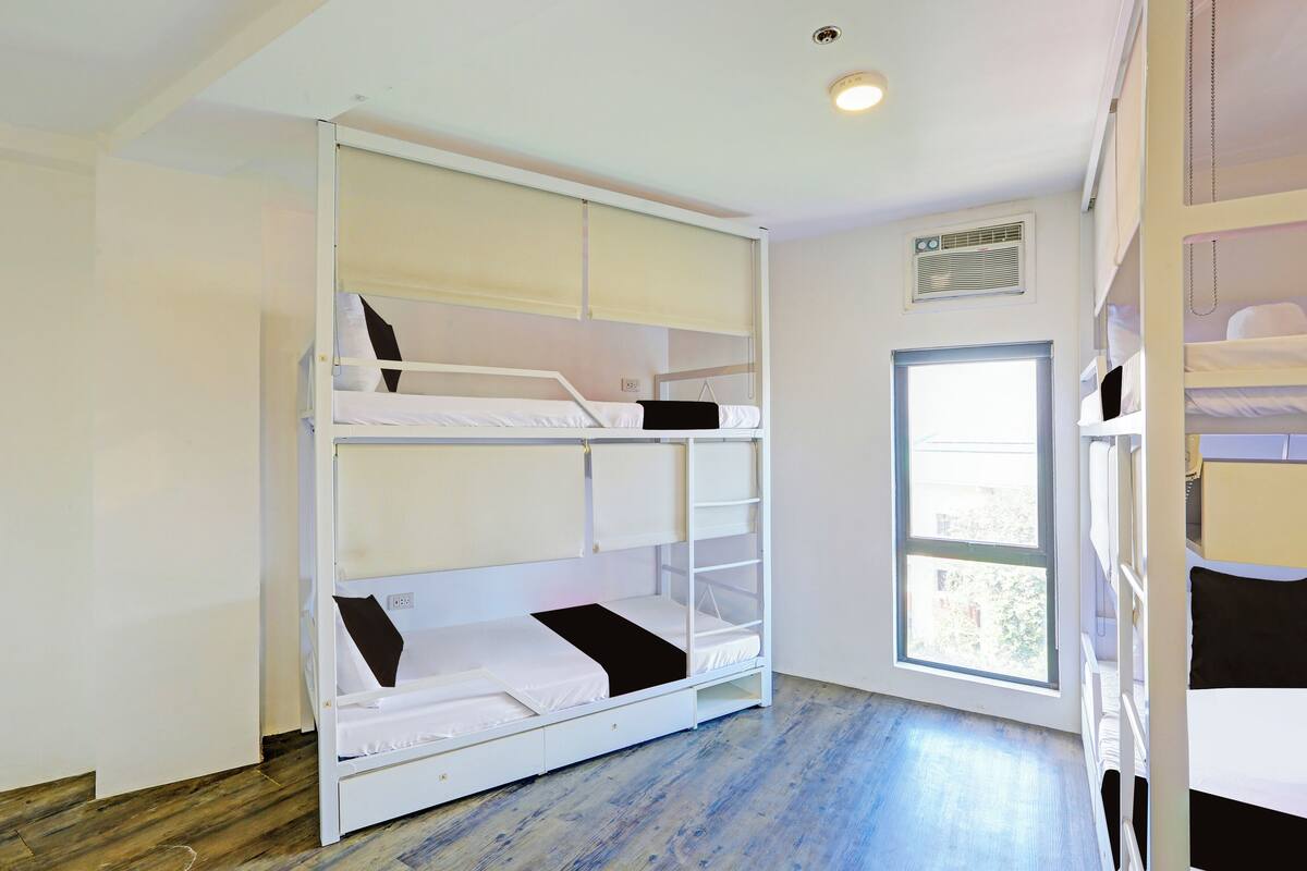 Habitación con literas, ventana, suelo de madera y una lámpara en el techo.