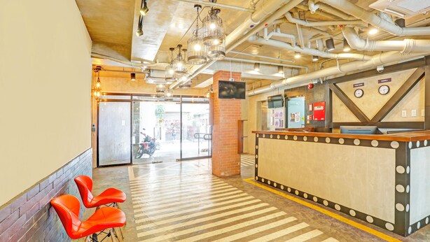 Una hall con reception, pavimento piastrellato e sedie rosse.