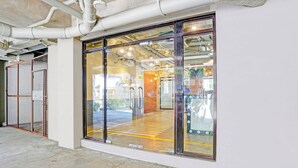 Ingresso di un edificio moderno con ampie porte in vetro, illuminazione interna visibile e pavimento in cemento.