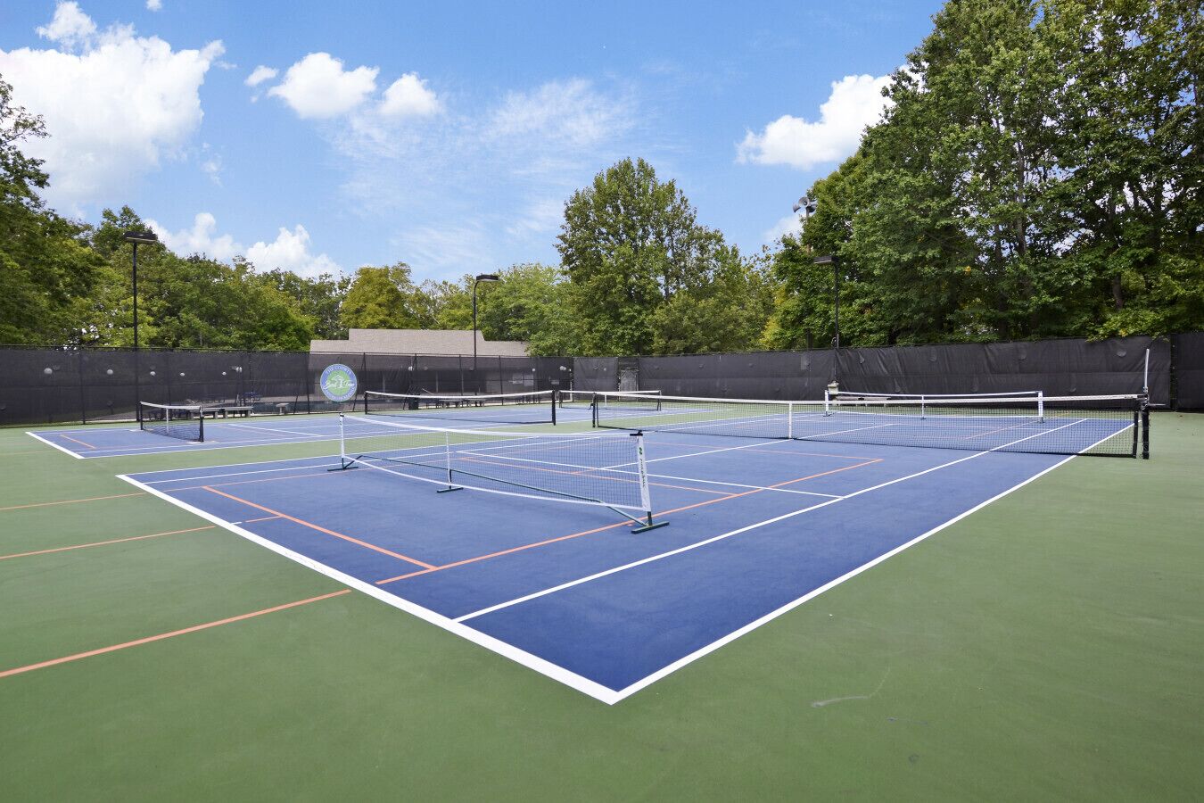An outdoor tennis court with multiple courts, surrounded by trees and a fence.