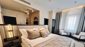 A modern hotel room with a large bed, bedside tables, a seating area with chairs, and a large window with curtains. - Sur Royals Hotel's (Diyarbakir)