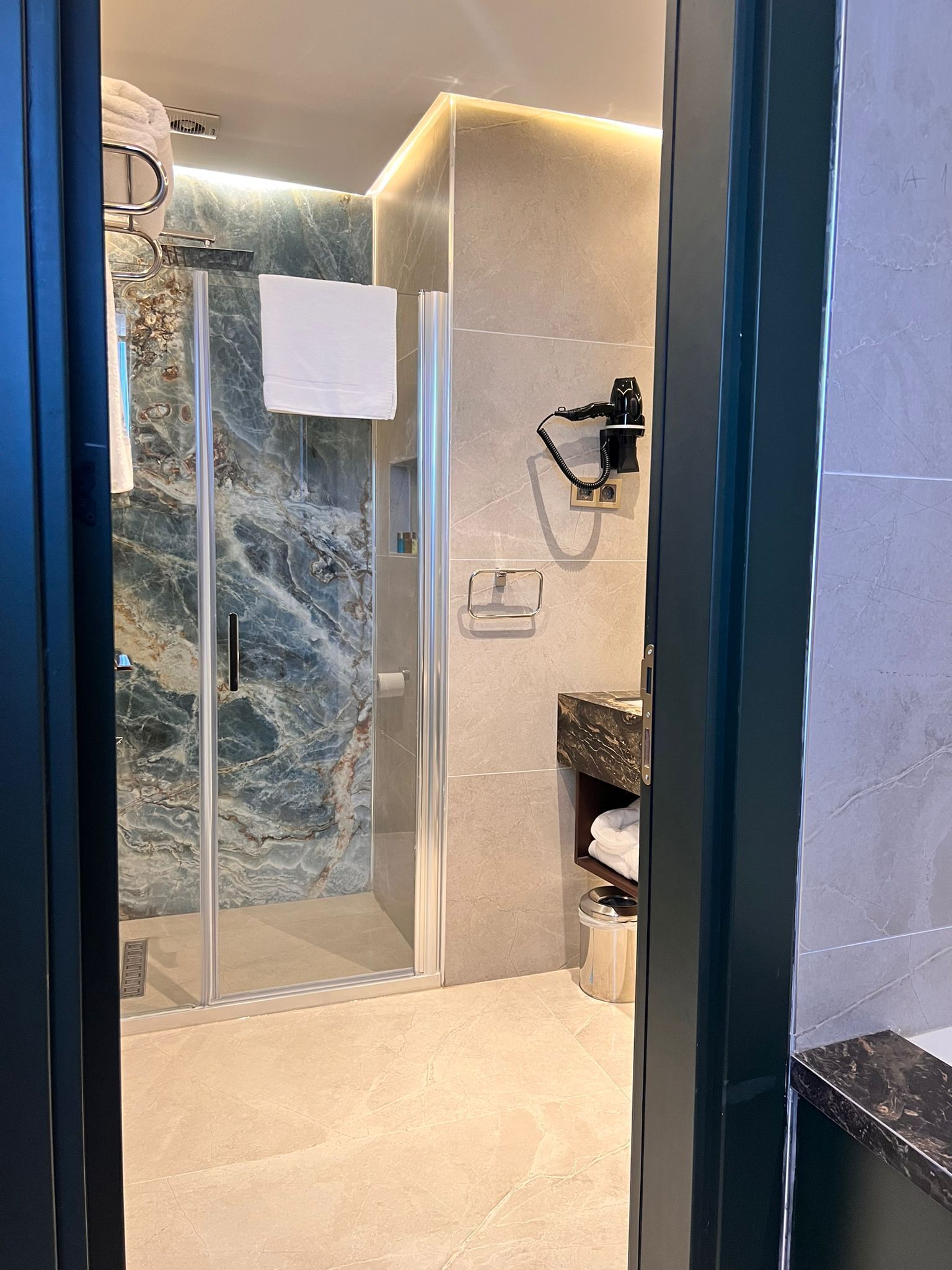 Een moderne badkamer met een douche met glazen wand, marmeren tegels, een handdoekhouder en een ingebouwd wastafelmeubel.