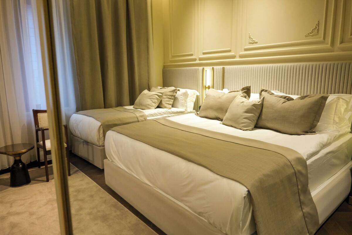 A hotel room with two beds, a small table, and a chair.