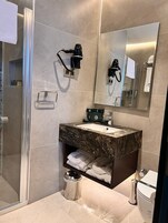 Un baño moderno con cabina de ducha de vidrio, lavamanos de mármol, inodoro y un espejo grande.